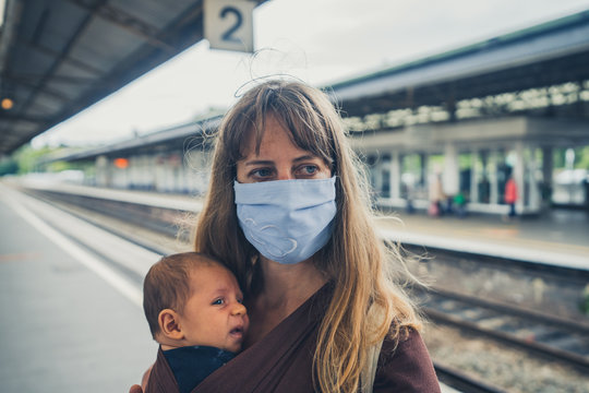 Young mother with baby in sling wearing face mask at train station