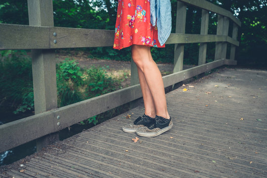 Legs of a young woman standing on a bridge in the woods