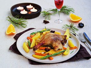 Roasted duck leg with potatoes, carrots and slices of orange on a ceramic plate