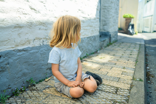 Little preschooler sitting on the pavement in a town