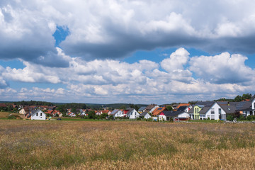 Obraz premium View across a field to a small village in Franconian Switzerland / Germany under a blue sky with white clouds