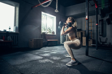 Obraz na płótnie Canvas Flexible, strong. Young caucasian female athlete training in gym, doing strength exercises, practicing. Beautiful girl works on her upper and lower body. Fitness, wellness, sport, healthy lifestyle