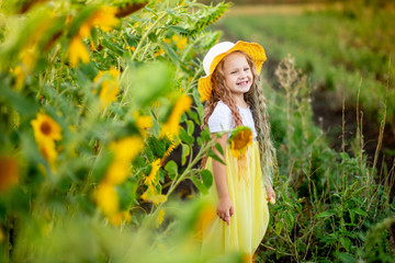 Obraz premium little happy girl in a field with sunflowers in summer