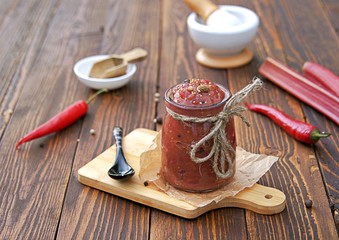 Spicy rhubarb chutney sauce in a glass jar on a wooden background.