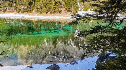 Fototapeta na wymiar Winter landscape of Austrian Alps with Green Lake in the middle. Powder snow covering the mountains and ground. Emerald color of water. Soft reflection of Alps in calm lake's water. Winter wonderland