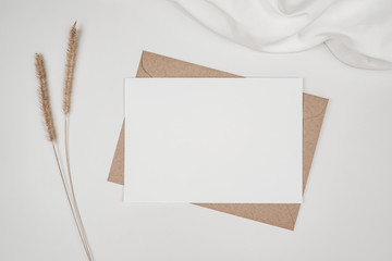 Blank white paper on brown paper envelope with Bristly foxtail dry flower and white cloth. Mock-up...