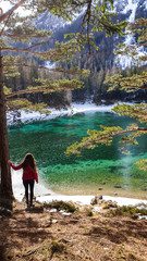 A woman standing at the edge of the cliff and enjoying the view on Alpine Green Lake in Austria. Powder snow covering the mountains and ground. Emerald color of water. Winter Wonderland. Adventure