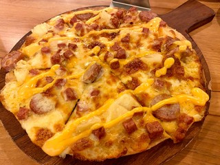 Hawaiian pizza with sausage, pineapple, ham, bacon, mozzarella cheese, on wooden plate