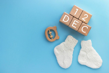 12 DECEMBER text on wood cubes, pair of cute knitted baby socks and wooden teether bear on blue background. Date of child birth. Newborn concept. Flat lay, top view with copy space.