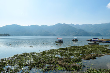 Fototapeta premium A view on Phewa Lake in Pokhara, Nepal. There are high Himalayan ranges around the lake. Few boats crossing the lake. Calm surface of the lake. Clear and sunny day. Undisturbed peace. Serenity
