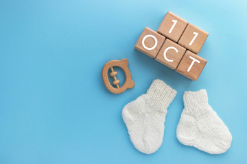 11 OCTOBER text on wood cubes, pair of cute knitted baby socks and wooden teether bear on blue background. Date of child birth. Newborn concept. Flat lay, top view with copy space.