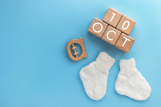 10 OCTOBER text on wood cubes, pair of cute knitted baby socks and wooden teether bear on blue background. Date of child birth. Newborn concept. Flat lay, top view with copy space.