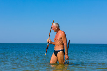 Man with a spear and a net in the sea looks out for a fish.