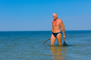 Man hunts with a homemade spear and a homemade helper in shallow water