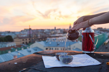 Hands pouring chinese tea into a clay teapot overlooking the sunset city