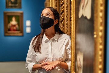Woman visitor wearing an antivirus mask in the historical museum looking at pictures.