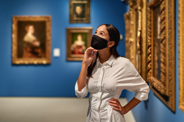 Woman visitor wearing an antivirus mask in the historical museum looking at pictures.