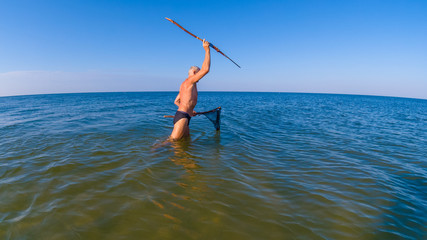 Man hunts with a homemade spear and a homemade helper in shallow water
