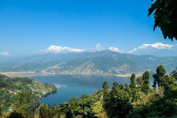 Fototapeta na wymiar Panoramic view on Phewa Lake from World Peace Pagoda in Pokhara, Nepal. In the back there are high, snow capped Himalayan chains, with Mt Fishtail (Machhapuchhare) between them. Serenity and calmness