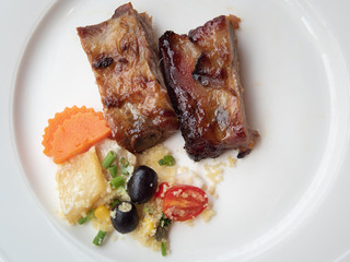 Pork ribs grilled with BBQ sauce and caramelized in honey served with a side dish on a white plate.