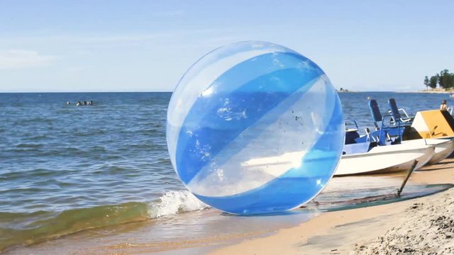 An empty water ball called a zorb or aquasphere, with other water activities, splashes on the waves, Zorbing extreme attraction for beach vacationers