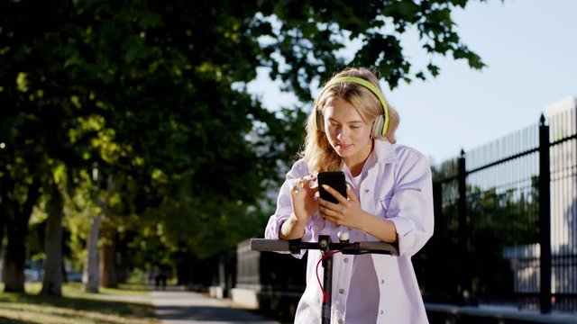 In the middle of modern street in a sunny day good looking young woman using her smartphone to typing some text she are so happy and smiling large she standing o her electric scooter