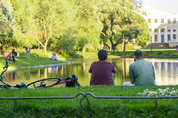 Two guys with bicycles sit on the shore of a pond in a summer park