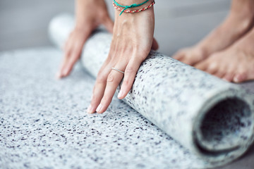 Frau/Yogalehrerin/Yogaschüler, die ihre Yogamatte aufrollt / einrollt