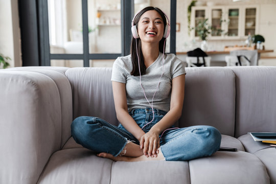 Image of woman listening music with headphones while sitting on sofa