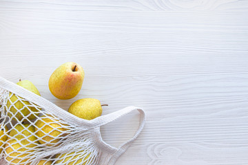 on a wooden light background lies a reusable white knitted eco-friendly bag with fruit pears