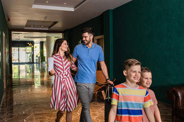 Smiling family of four enters to the hotel lobby to check in at the reception for vacation.
