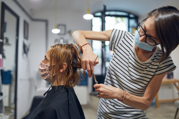 Hairdresser and customer in a salon with medical masks during virus pandemic. Working with safety mask.