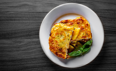 Traditional greek moussaka in white plate on black wooden table background