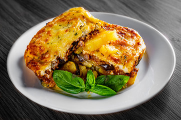 Traditional greek moussaka in white plate on black wooden table background