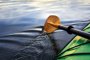 Boat oar and part of green kayak in the water and splashing water at evening river at sunset - obrazy, fototapety, plakaty