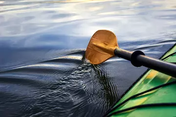Foto op Canvas Boat oar and part of green kayak in the water and splashing water at evening river at sunset © watcherfox