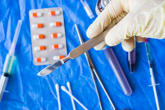 Hand with glove holding surgery blade, drugs, ampule,needle and blood tube