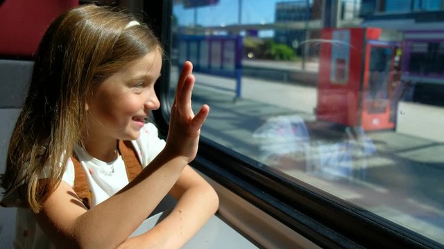 The girl travels by train and looks out the window, she waves her hand.