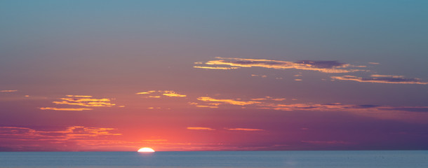 Naklejka premium Beautiful sunset at the sea. Young people walk along the beach. People are watching the sunset. Sea and red-yellow sky. Silhouettes of people on the background of the sunset. In the evening by the sea