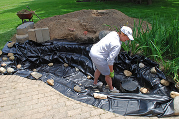 Woman working on vinyl liner of the pond for a water feature project in the backyard