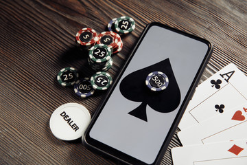 Online poker casino theme. Gambling chips, smartphone and playing cards on wooden table.