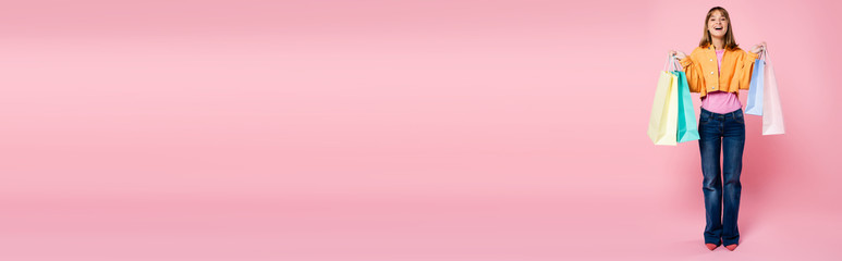 Panoramic concept of young woman holding colorful shopping bags on pink background