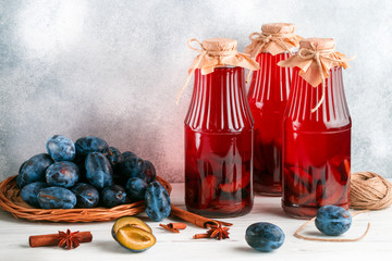 Homemade plum compote with cinnamon and star anise. Delicious healthy vitamin drink. Jars and fresh berries on a light wooden table. Home preparations. Selective focus, copy space