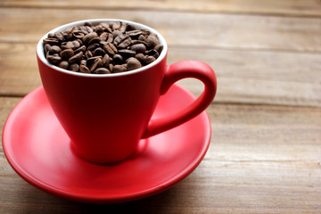 Cup of coffee beans on a wooden table. Close-up of coffee beans in a red cup on wood background with copy space.