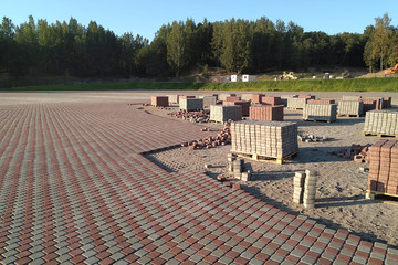 Laying the area with red and gray paving stones. Construction site, paving slabs on wooden pallets. The idea is to improve the urban environment. Horizontal photo.