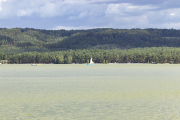 View of the lake surface, hills, clouds in windy weather with one yacht