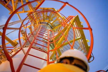 Bottom up pov of oil worker on an industrial steel ladder with safety cage. Heavy industry gas and...