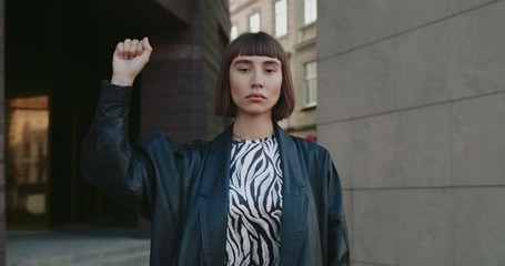 Young attractive woman raising hand with clintched fist up while standing at street. Millennial girl activist supporting movement and fighting for human rights. Concept of protest