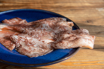 Two squid carcasses on a blue plate on a wooden background