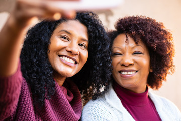 Cheerful black mother and daughter with cell phone taking a self portrait outside. Relationship, leisure, enjoyment concept.